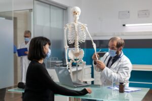 Orthopedic doctor explaining bones pain on human skeleton to patient